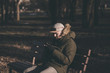 © jozzeppe777 - stylish bearded man in a winter jacket sitting on a bench with a smartphone