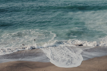 Big wave coming to the shore. Pair of siwmmers in the ocean.