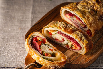 Traditional Italian Stromboli stuffed with cheese, salami, red pepper and spinach. Photo in a dark style.