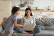 © fizkes - Mother seated on couch using computer her active son running