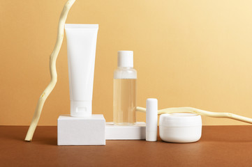 Wall Mural - Facial and body care cosmetics bottles composition on brown background. Gel tube, lipstick, cream jar unbranded blank packages decorated with wooden sticks. Skincare products advertising