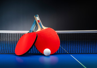 Ping pong rackets and balls on a blue table with net.