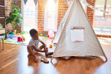 Beautiful african american toddler putting on shoes outside tipi at kindergarten