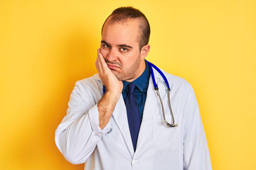 Poster - Young doctor man wearing coat and stethoscope standing over isolated yellow background thinking looking tired and bored with depression problems with crossed arms.