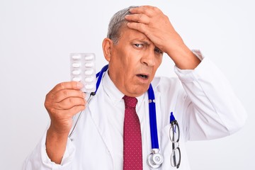 Poster - Senior doctor man wearing stethoscope holding pills over isolated white background stressed with hand on head, shocked with shame and surprise face, angry and frustrated. Fear and upset for mistake.