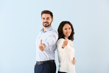 Portrait of young business people showing thumb-up gesture on color background