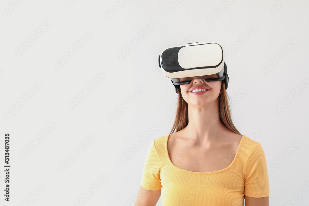 Young woman with virtual reality glasses on light background