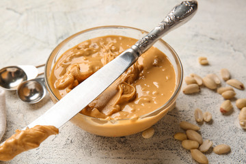 Bowl with tasty peanut butter and knife on white background