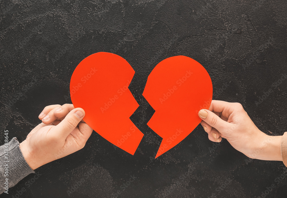 Hands of couple with broken heart on dark background. Concept of divorce