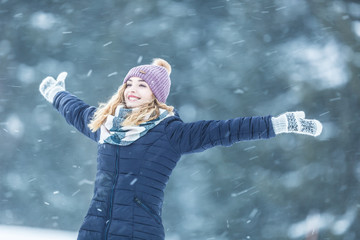 Wall Mural - Happy young woman in warm clothing enjoying winter snowfall