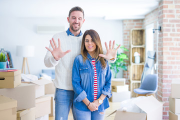 Sticker - Young beautiful couple standing at new home around cardboard boxes showing and pointing up with fingers number ten while smiling confident and happy.