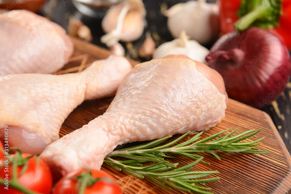 Raw chicken drumsticks on wooden board, closeup