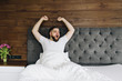 © Anastasiia - Young caucasian bearded man yawning and stretching in his bright modern bedroom in the morning