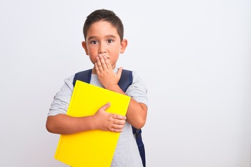 Canvas Print - Beautiful student kid boy wearing backpack holding book over isolated white background cover mouth with hand shocked with shame for mistake, expression of fear, scared in silence, secret concept