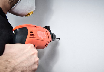 Poster - The worker uses a drill. Drilling a hole in the wall. A man holds a red drill in his hand, doing home renovation, refreshing the apartment, home.