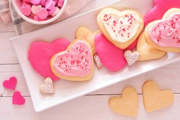 Aufkleber - Heart shaped Valentines Day cookies with pink and white icing and sprinkles. Overhead view on a serving plate against a white wood background.