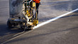 Low section of road worker with thermoplastic spray road marking machine working to paint traffic white  line with steam and railway track crossing on asphalt road surface 