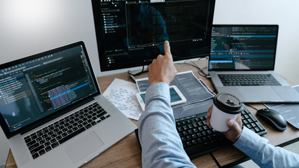 Wall Mural - programmer working on computer in it office typing data coding in software and checking code on comp