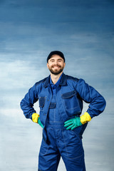  Thumb up. Young handsome man with a beard in a blue working uniform for cleaning rooms smiles isolated on blue background