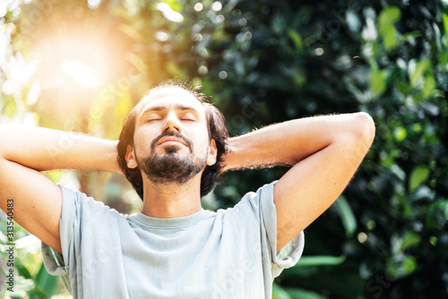 Fotomural A bearded man is meditating outdoor in the park with face raised up to sky and eyes closed on sunny summer day