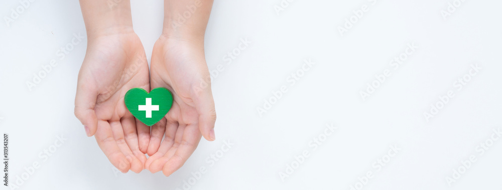 Hands holding a beautiful green heart with hospital white cross symbol on it showing a concept of Health care service, cancer treatment and heart surgery. Banner top view Isolated on white background. - obrazy, fototapety, plakaty 