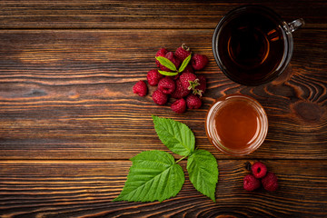 Wall Mural - Cup of black tea with raspberry and honey on dark wooden background.