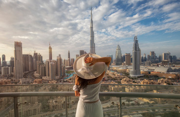 Woman with a white hat is standing on a balcony in front of the skyline from Dubai Downtown