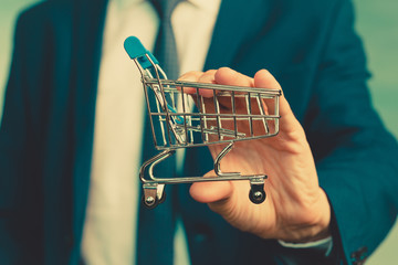 Male hands of a businessman in a blue suit with a tie hold a little shopping trolley.