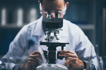 Wall Mural - young scientist looking through a microscope in a laboratory. young scientist doing some research.