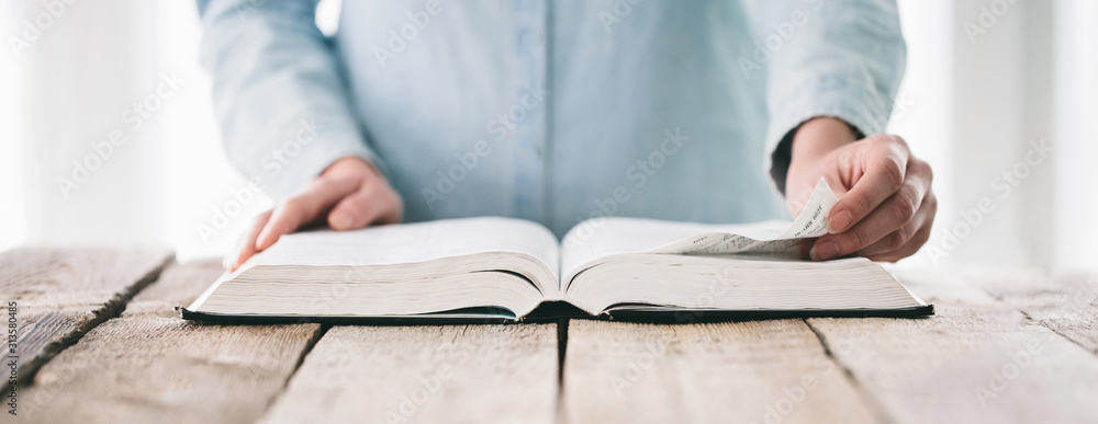 Hands turning the page of a bible. Woman reading a big book or a Bible - obrazy, fototapety, plakaty 