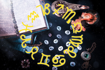 Astrology and esotericism. On a black background lie fortune-telling runes, a book, an amulet, and a candle. Light. Top view. Yellow zodiac horoscope on the foreground