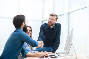 smiling co - workers shaking hands with each other at an office meeting.