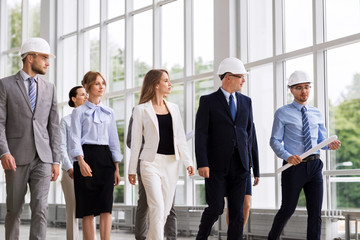 architecture and construction business concept - happy group of architects in helmets with blueprint walking along office building