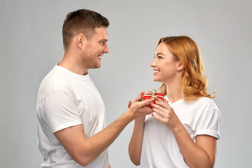 Poster - relationships, holiday and valentines day concept - happy couple in white t-shirts with christmas gift over grey background