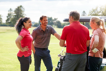 Group Of Male And Female Golfers Standing By Golf Buggy On Course