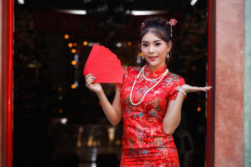 Concept to celebrate Chinese New Year : Chinese woman in a red cheongsam (qipao) dress holding red envelopes (hong bao) at shrine.