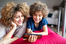 Mother And Son Watching A Video On Smartphone, Lying On Big Pillow