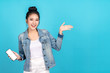 © ChayTee - Happy asian woman feeling happiness and standing hold smartphone other hand open on blue background. Cute asia girl smiling wearing casual jeans shirt and connect internet shopping online and present