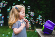 © Cavan Images - A little girl stands in front of a bubble machine.