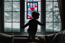 A Little Boy Stands In Front Of A Snowy Window.