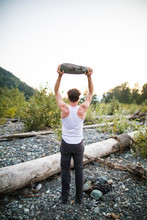 Rear View Of Man Lifting Rock Above Head During An Outdoor Workout.