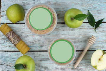 Green apples on a light table and a spoon spindle with a beeswax candle, jars with a product or cosmetics, top view