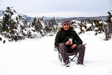 Handsome Young Man Is Sitting On Camping Chair, Drinking Coffee With Thermos Mug And Enjoying Snow In Winter Season. Winter In Eskisehir.