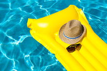 Hat And Sunglasses Resting On Bright Yellow Inflatable Raft Floating In Blue Swimming Pool