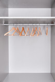 Fototapeta Na ścianę - row of lacquered wooden light hangers for clothes hangs in wardrobe on metal rod. There's empty shelf on top. Accessories made of environmental material
