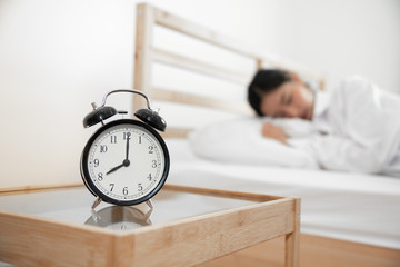 Closeup alarm clock with sleeping woman in bed room. Lazy time in holiday concept.