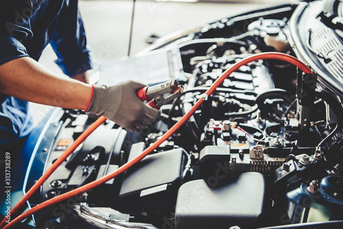 Fotografía Car mechanic holding battery electricity trough cables jumper and checking to maintenance vehicle by customer claim order in auto repair shop garage