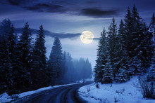 Country Road Through Forest At Night. Misty Winter Weather In Full Moon Light. Snow On The Roadside. Cloudy Sky