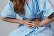 © ztony1971 - Close up of woman mid-body in hospital gown holding her stomach having abdominal pain, menstrual pain or food poisoning isolated in gray background, concept healthcare insurance, food poisoning,