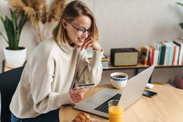 Canvas Print - Photo of joyful blonde woman holding credit card and using laptop